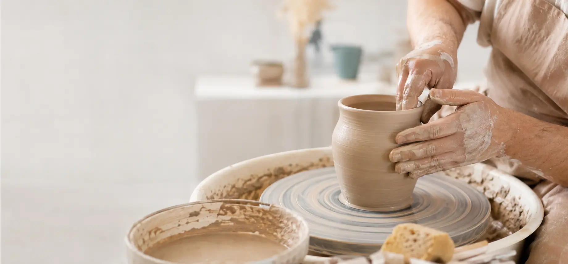 Hands forming a stoneware vessel on a pottery wheel